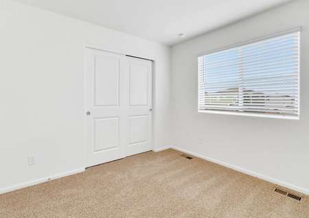 Guest bedroom with tan carpet and closet with sliding doors.
