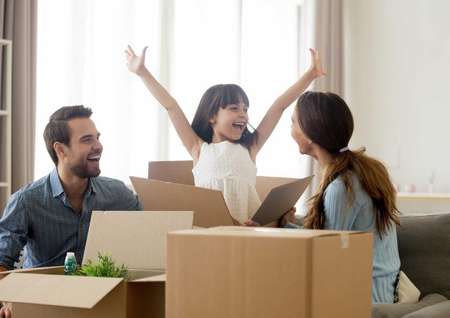 Stock image of family unpacking boxes, little girl excited with hands in the air.