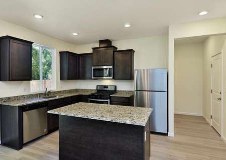 Beautiful modern kitchen with dark brown cabinets, granite counters, island, stainless appliances and a window.