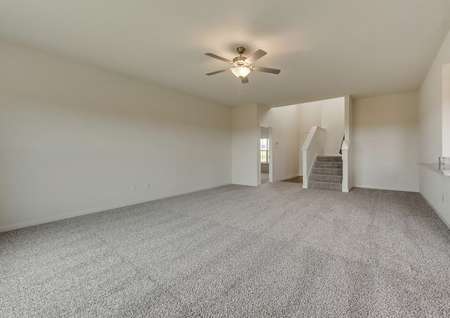 The living room has brown carpet, white walls and comes with a ceiling fan installed.