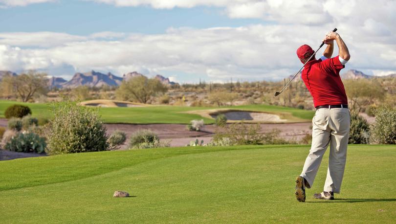 Phoenix, Arizona desert landscape golf course with man teeing off, green fairways, and desert plants