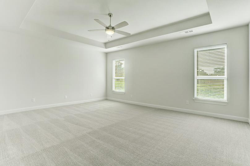 The master suite has light carpet, white walls and a ceiling fan.