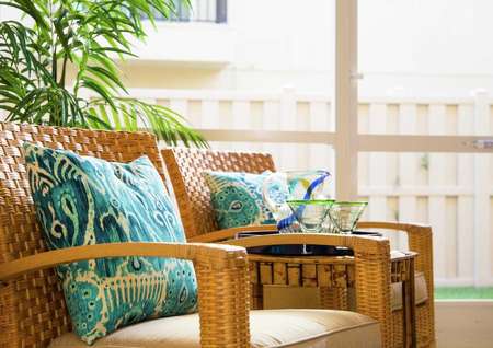 Sea Forest Beach Club model home completed with wooden chairs that have turquoise pattern pillows and beige cushions, table with glasses sitting on it, and a house plants in the background