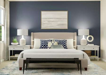 Rendering of the master bedroom decorated
  with a navy accent wall and ark blue geometric pillows. The sand colored bed,
  white nightstands and distressed rug pair with the blue elements and dark
  grey bench at the foot of the bed.