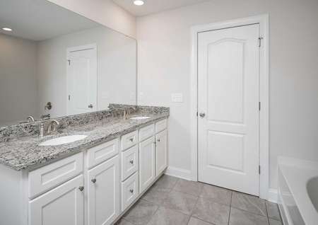 A tile-floored bathroom in the Kiawah floor plan with white double sink vanity and granite countertops.