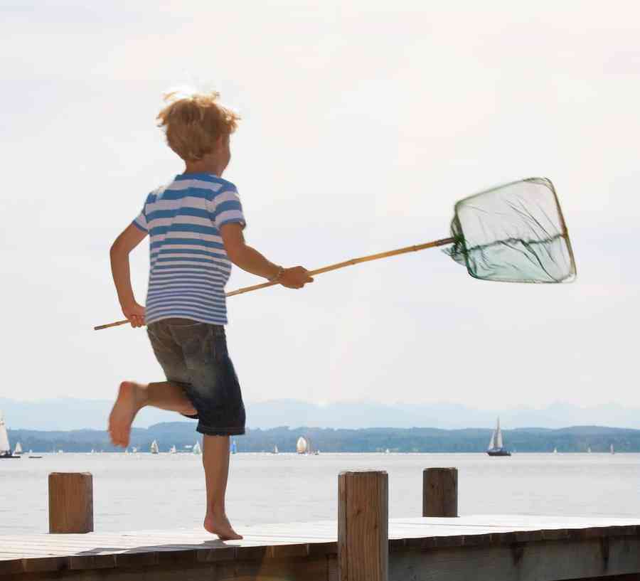 Stock photo of a boy in shorts running on a dock with a fishing net.