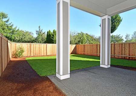 Photo of a fenced back yard with green grass from underneath a covered back patio.