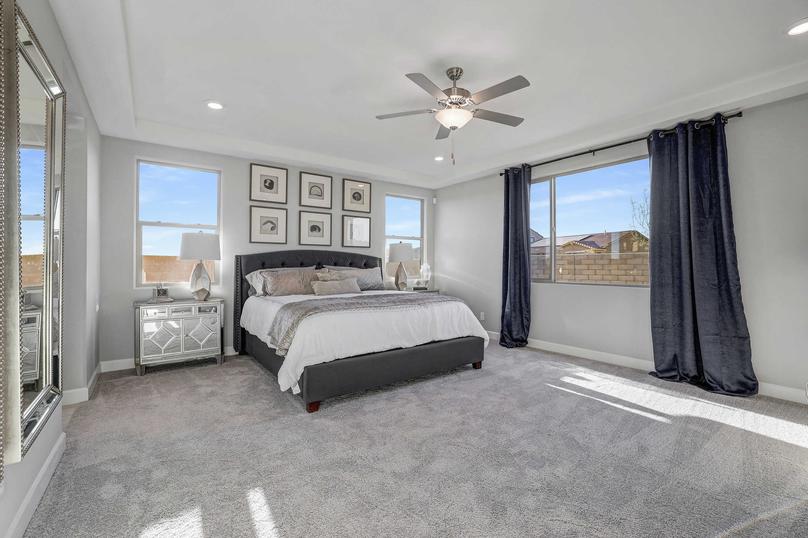 Staged master bedroom with ceiling fan and several windows