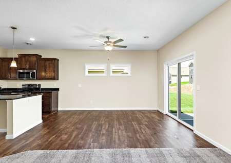 Photo of the dining room with brown plank flooring and sliding glass door open to kitchen with island and family room with carpet.