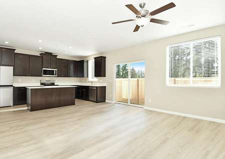 Open kitchen, dining and family room with plank flooring, ceiling fan, dark brown cabinets and stainless appliances.