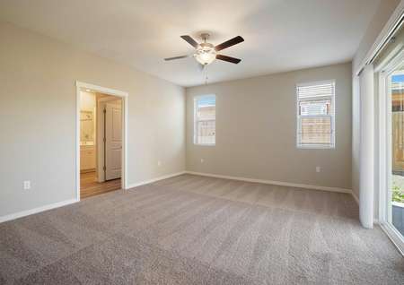 The master suite has light brown carpet, tan walls and a ceiling fan.