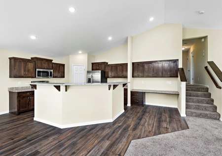 Photo of an open kitchen with vaulted ceilings, an island with a breakfast bar, recessed lighting and brown cabinets.