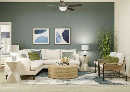 Rendering of the spacious living room
  with light wood-look flooring, a blue accent wall and a ceiling fan. The room
  is decorated with a white sectional couch, two end tables, a coffee table and
  two armchairs. 