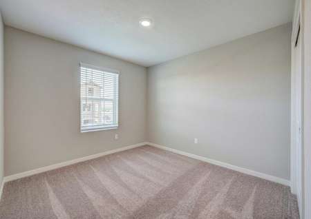 A secondary bedroom upstairs in the Kennedy floor plan with carpet floors, white baseboards and tan walls.