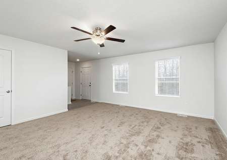 Spacious family room with carpet and a ceiling fan plus two windows.
