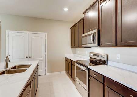 The Santa Maria model home's kitchen with dark brown cabinetry, crown molding, tile flooring and stainless steel appliances