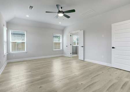 Spacious master bedroom with large windows, a ceiling fan, and wood flooring. 