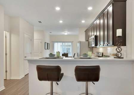 Pine model home kitchen area with two brown-backed barstools, a candle, and place settings on the granite countertop