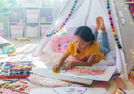 Young girl coloring with crayons in a colorful room.
