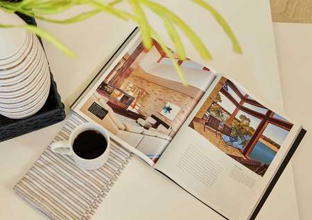 Staged image of coffee table with open book, plant vase, and cup of coffee.