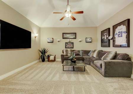 Media room with sectional, large tx, ceiling fan and football jerseys. 