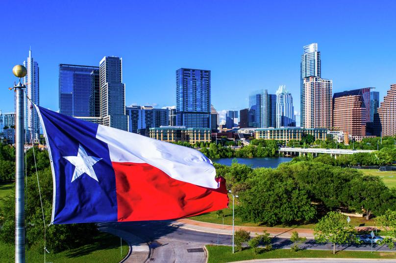 Austin, Texas Cityscape shot with numerous skyscrapers in the background, green lush park in the front and a Texas flag hanging on a flagpole
