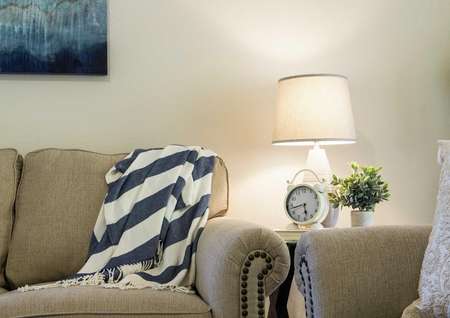 Staged home with light brown colored modern sofa, white and blue blanket and painting hanging on the wall.