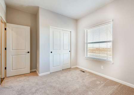 Guest bedroom with tan carpet and closet with sliding doors.