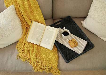 Trace living room with book, coffee cup, and yellow shawl on couch