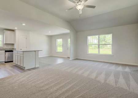 Open living room with carpet, window to backyard, ceiling fan looks into kitchen with island and breakfast room.