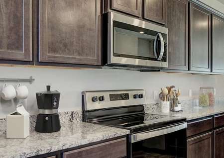 Staged kitchen with stainless steel appliances, brown cabinets and brown flooring.