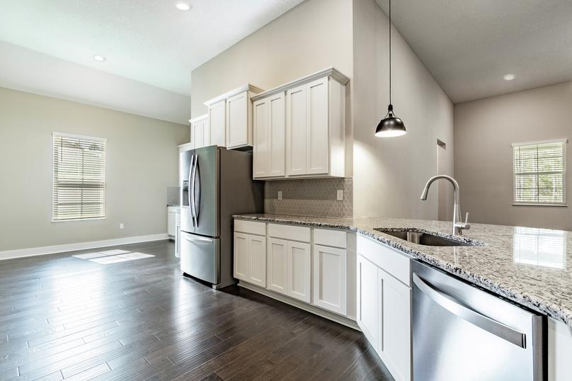Chef-ready kitchen with granite countertops, white cabinetry, a gray backsplash, wood flooring and stainless steel appliances.