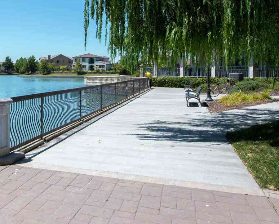 A walkway along a lake in the Bridgeway Lakes community a fence in between them.