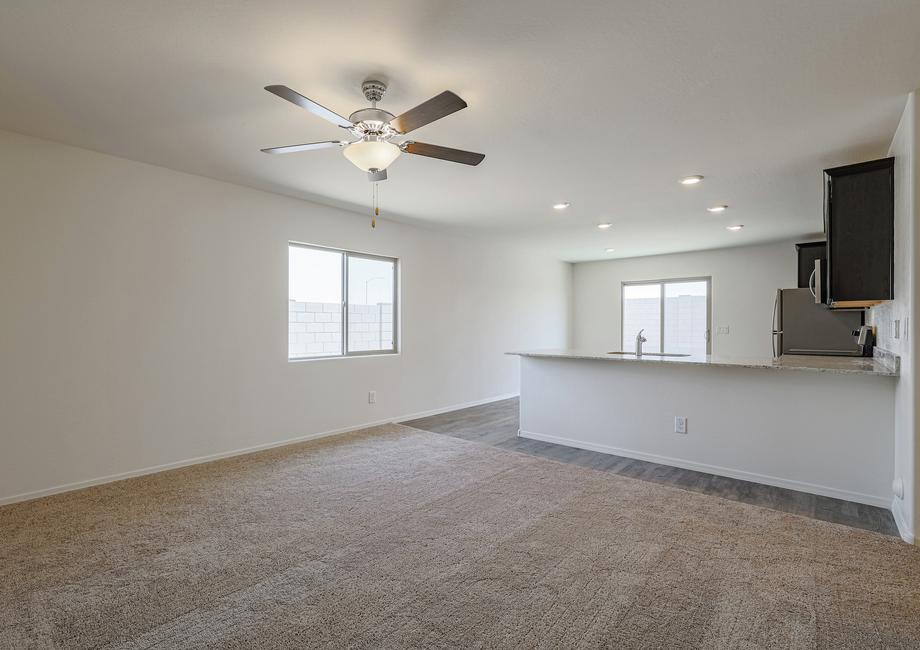 Open family room with tan carpet, a ceiling fan and access to the kitchen.