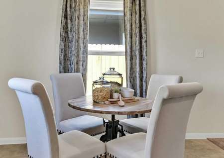 Walnut staged dining area with four white chairs around a small wooden table and tall drapes hanging over the window in the background