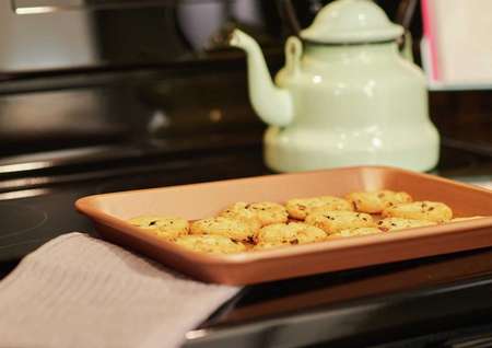 Staged photo stovetop detail with cookies in tray, kettle on black electric cooktop.