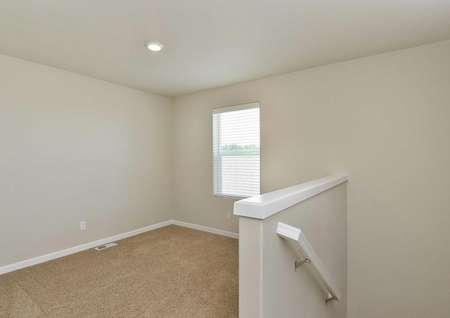 The Northwest Cypress game room is shown with brown carpet and short wall with stair rail.