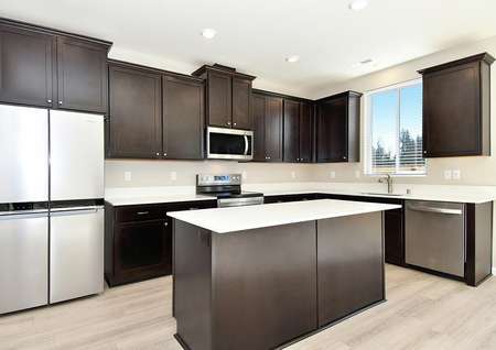 Close up of kitchen with dark brown cabinets, white quartz counters and stainless steel appliances and a window.
