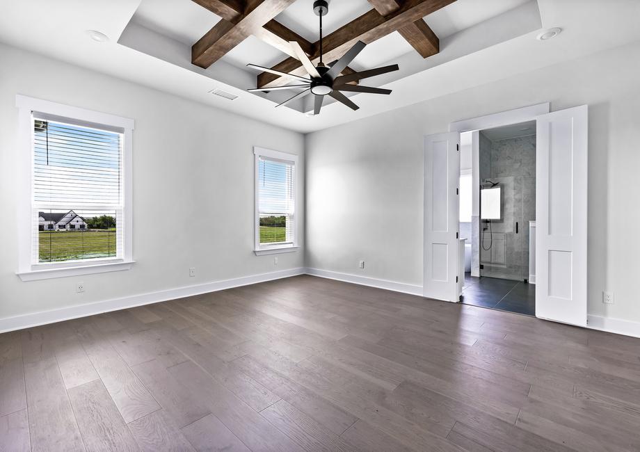 Expansive master bedroom with windows, a ceiling fan, and wood flooring. 