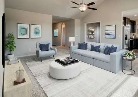 Staged living room with blue couch, vaulted ceiling and access to the kitchen.