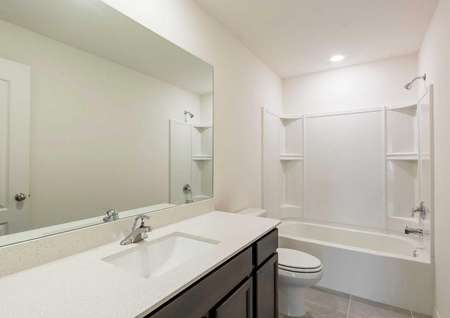 Anastasia bathroom with travertine countertop, large vanity mirror, and white fixtures