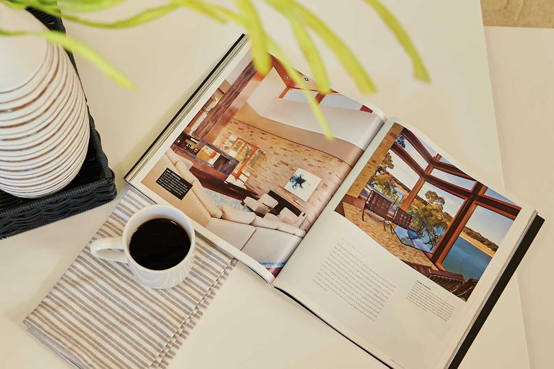 Staged image of coffee table with open book, plant vase and cup of coffee.