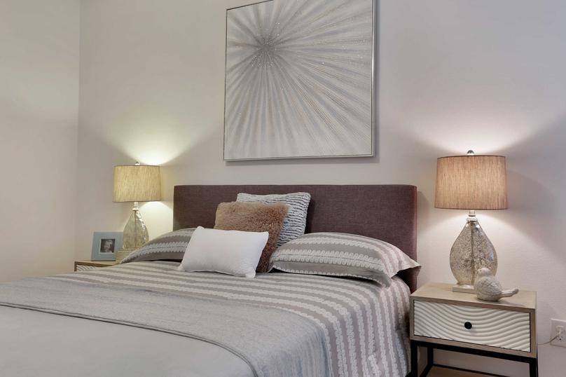 Bed with gray linens, side tables with lamps and a decorative wall hanging.