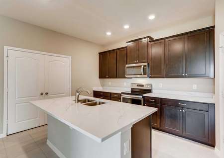 The kitchen in the Santa Maria model home. Quartz countertops, a large kitchen island, stainless steel appliances, large pantry and upgraded dark brown cabinets