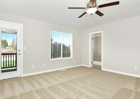Photo of primary bedroom with carpet, ceiling fan and door leading to private balcony.