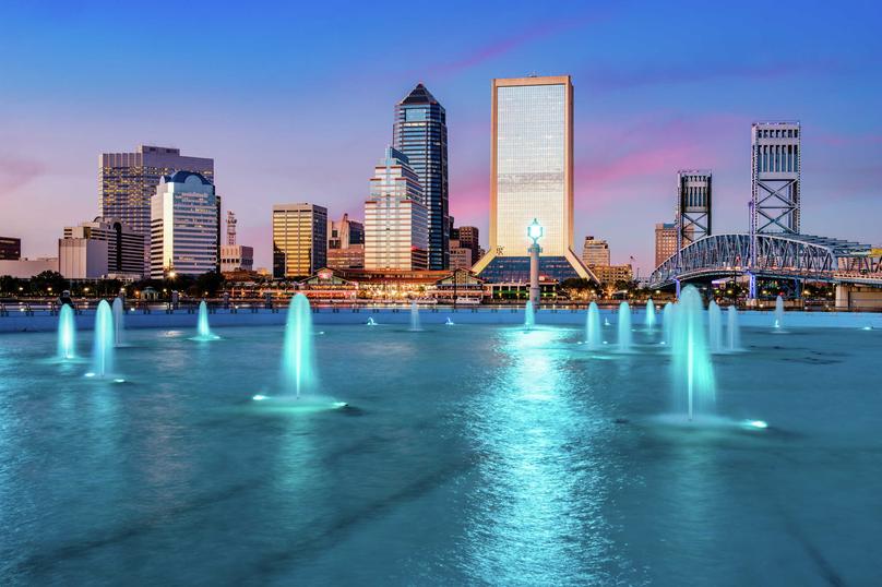 Jacksonville, Florida downtown city view at dusk with blue-light lit water features, skyscrapers in the background, and blue drawbridge