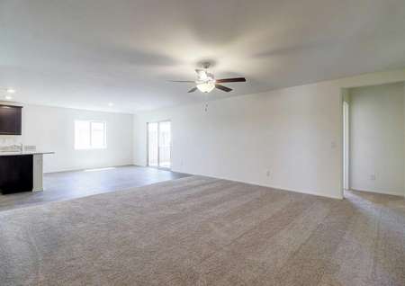 The spacious living room in the Guadalupe floor plan with carpet flooring, white walls and a ceiling fan with light.