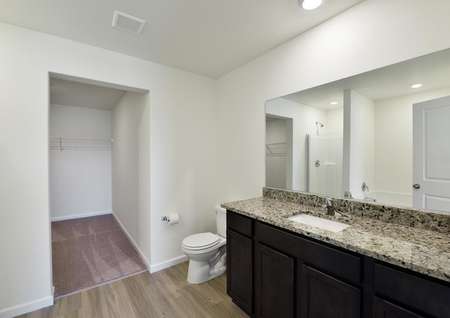 Spacious primary bathroom with extra long vanity with granite countertop, single sink, dark brown cabinets and plank flooring.