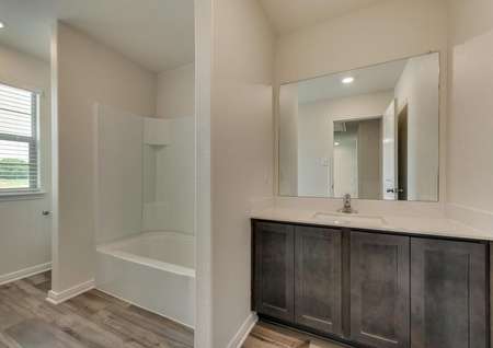 The secondary bath has wood style flooring, brown cabinetry and plenty of space.