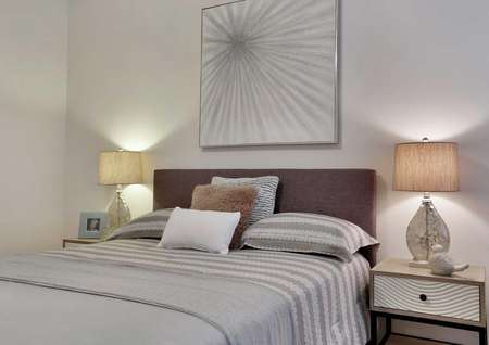 Bed with gray linens, side tables with lamps and a decorative wall hanging